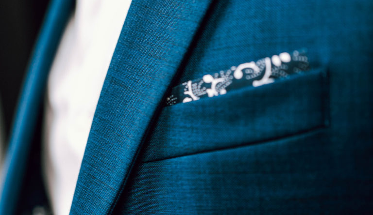 Close up photo of a mans blue suit jacket with a top pocket handkerchief