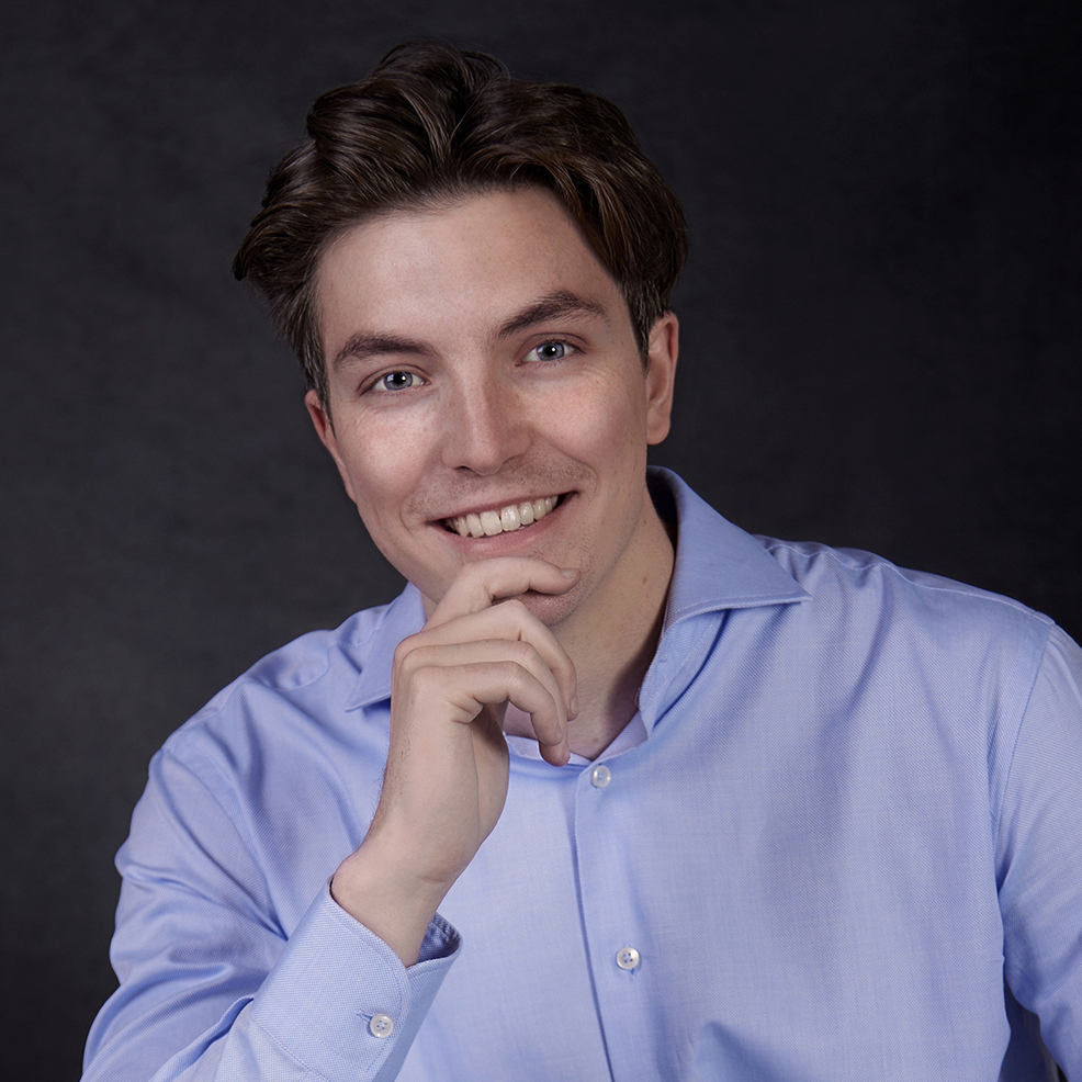 Young man wearing smart blue shirt with his hand on his chin against a dark backdrop