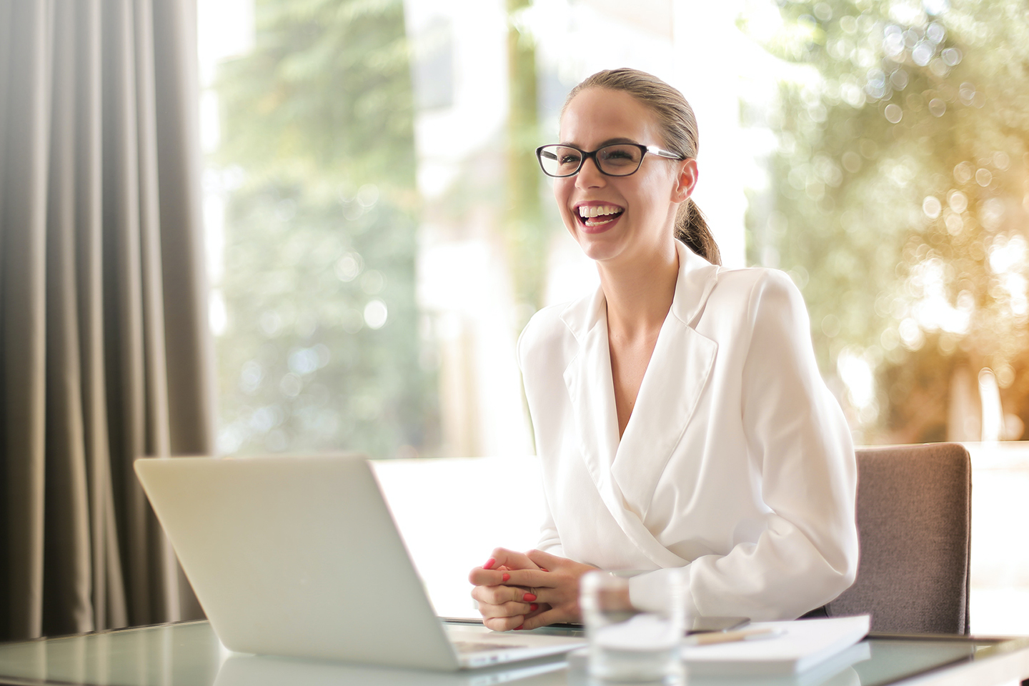 Young lady wearing white shirt sitting behind a desk with a laptop smiling